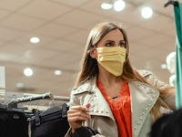 Woman shopping in fashion store wearing face mask looking at some clothes