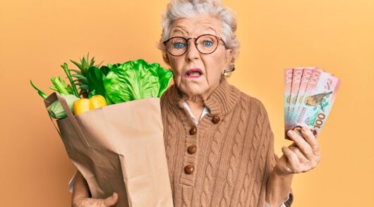 senior woman holding groceries and NZ dollars