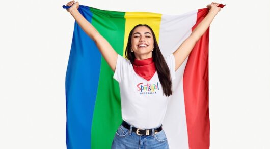 A campaign image showing a brunette model in a Sportsgirl graphic t-shirt holding a striped flag