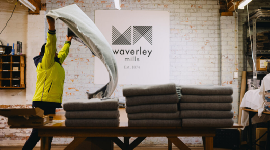 A worker folds a woven blanket in front of a sign saying Waverley Mills