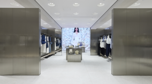 The symmetrical interior of a Zara store with reflective metal fixtures and surfaces and a digital screen showing a model.