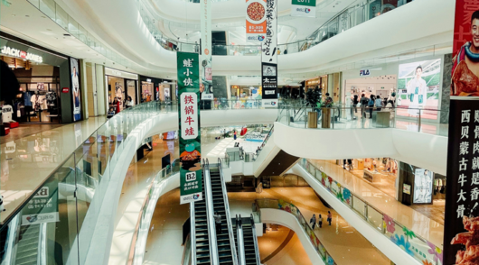 An interior shot of a shopping mall in China, showing escalators and storefronts.