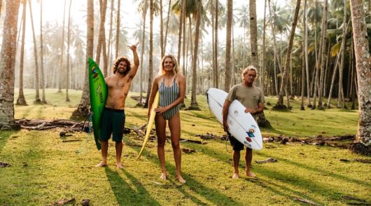 Three surfers with boards beneath palm trees