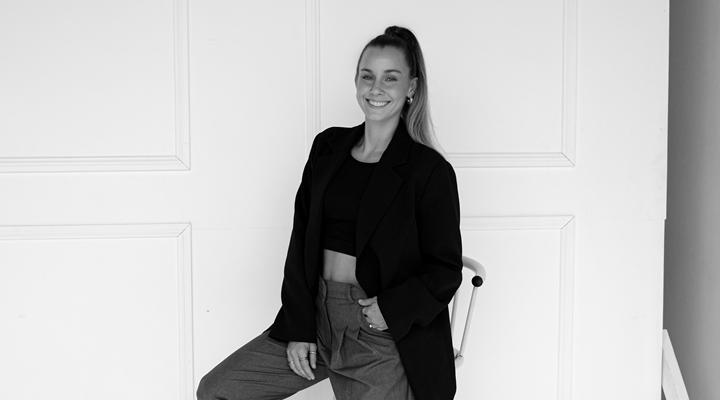 A black and white image of Kim Zorn sitting on a stool with her hand in her pocket