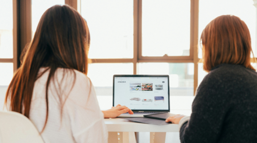 Two women sitting at a table looking at a laptop screen