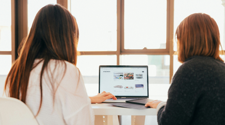 Two women sitting at a table looking at a laptop screen