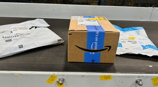 a brown cardboard amazon box with blue tape on a conveyor belt