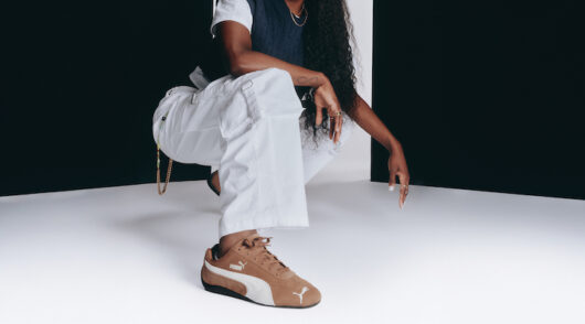 An image of Flau’jae Johnson crouching down to the ground, wearing a brown and white pair of Puma Speedcat sneakers.