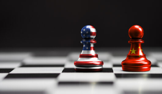 Chess pieces resembling the US and Chinese flags on a chessboard and set against a black background.