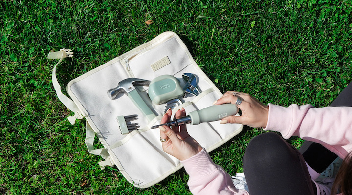 A woman’s hands holding tools from a pale green Tinkr tool kit.