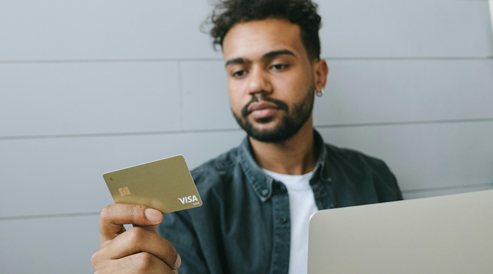 A Man in Black Denim Jacket Looking at the Visa Card He is Holding