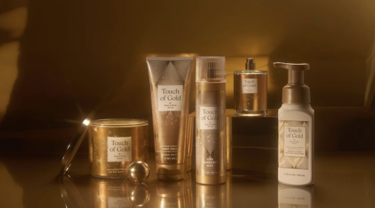 Several products from Bath & Body Works’ Touch of Gold’ collection set against a dark gold background.