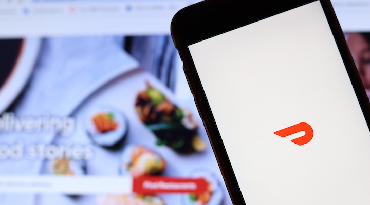 A superimposed image of a smartphone featuring the DoorDash logo held in front of a computer screen.