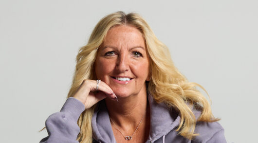 A headshot image of Hannah Mercer wearing a purple hoodie against a gray background. ]\\