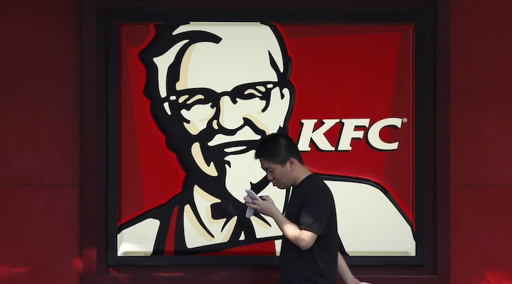 A man walks past a logo of KFC