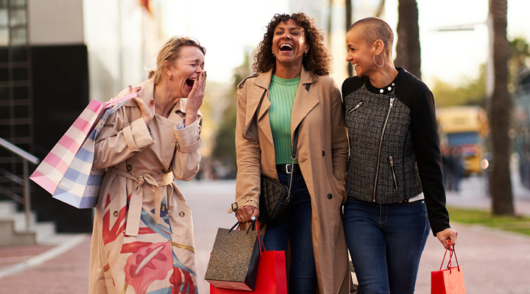 Three women with shopping bags walking and laughing.