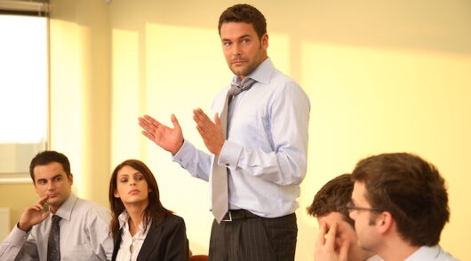 Several men and women sitting in a boardroom with serious expressions on their faces.