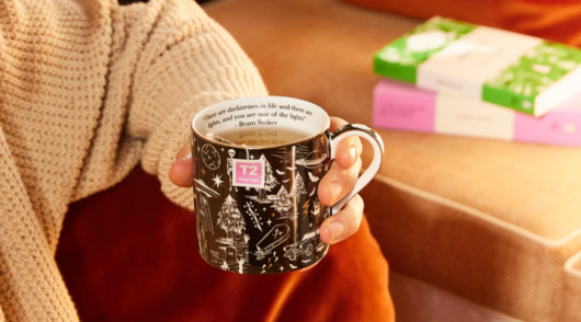 Hand holding T2 tea mug on sofa.