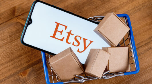 A phone showcasing the Etsy logo in a mini cart with cardboard boxes.