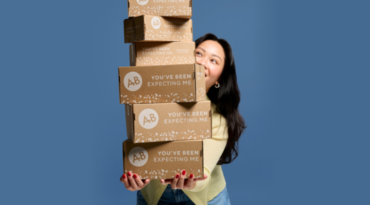 adore beauty campaign image showing woman carrying a stack of branded boxes
