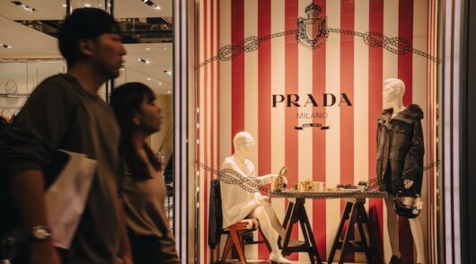 Mannequins in Prada store window with pedestrians passing by in Osaka.